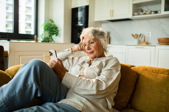 Senior woman relaxing on sofa using smartphone at home