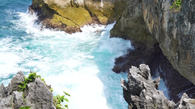Ocean waves crashing against rocky tropical cliffs with white foam water.