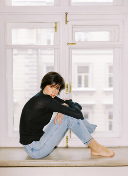 Woman Sitting on a Windowsill Wearing Black Top and Blue Jeans