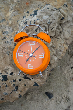 Orange alarm clock on rough stone surface for time management and daylight saving time concept