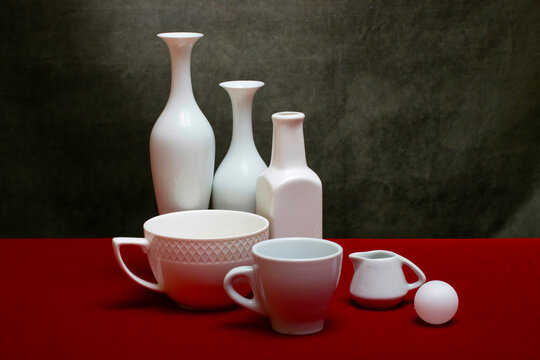 Still life with white dishes on a table with a red cover.