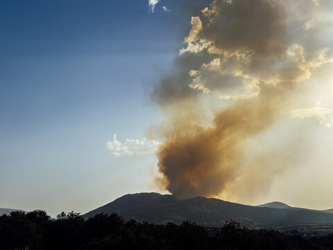 Smoke plume rising over mountain landscape at sunset during a fire