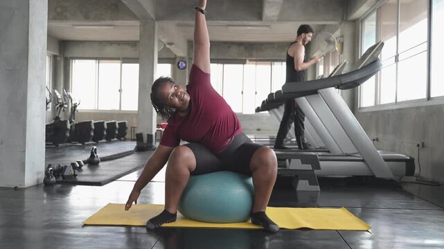 Woman performs a stretching exercise with a stability ball on a gym mat, representing flexibility training, fitness routine, balance, active lifestyle, physical wellness, and healthy exercise.