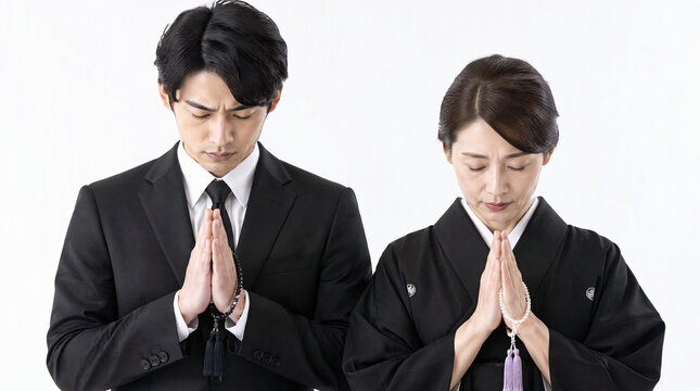 数珠を持ち祈る喪服姿の男女