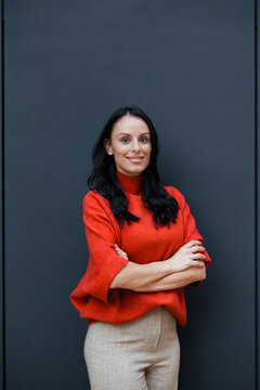 Confident professional woman standing against a dark background, smiling and looking at the camera, showing determination, success, and business expertise