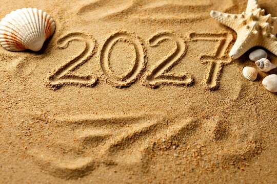 Year 2027 written in sand with seashells and starfish on beach for summer holiday vacation or new year greeting card design themed around seasonal ocean trip.