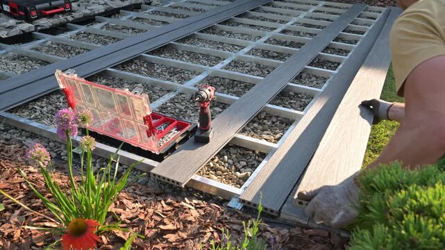 Worker laying gray composite deck boards over a support frame