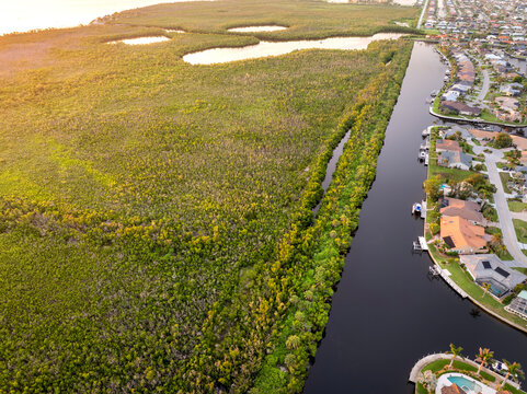 Sunset aerial panorama of Florida Gulf waterfront. Wealthy neighborhood with elegant houses, premium living and palm-lined canals.