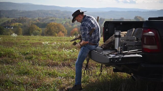 Man handling an axe while sitting on a pickup truck tailgate