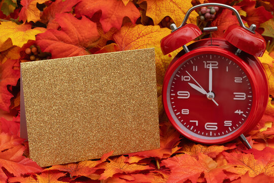 Autumn scene with fall leaves and alarm clock and greeting card for your autumn message