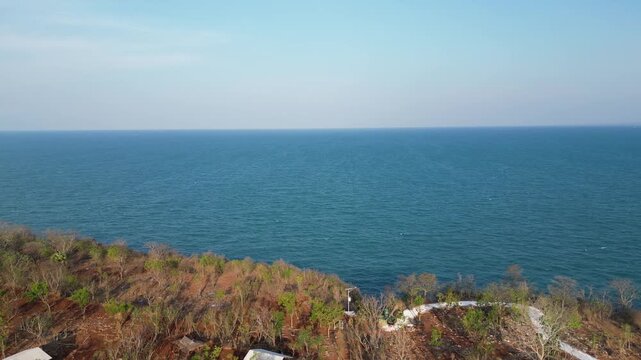 Aerial video of coastal cliff, dry vegetation and calm blue sea horizon on Gili Iyang, the Oxygen Island, Sumenep, Madura, East Java, Indonesia