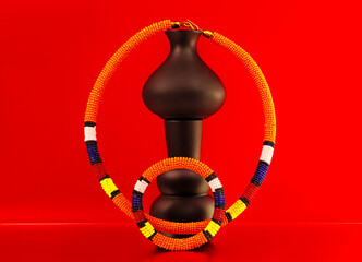 ibrant African beaded bracelet featuring bold orange, yellow, red, blue and white patterns, styled with sculptural vases against a striking red and orange backdrop for a colourful fashion still life. © Valerie