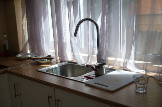 Kitchen sink and faucet beside a window with dishes and cutting board on the counter