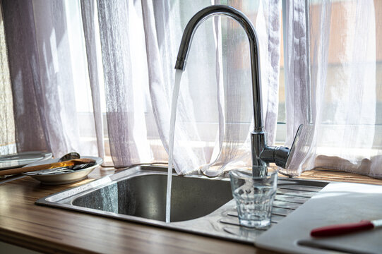 Water running from a kitchen faucet into a glass beside the sink during daytime