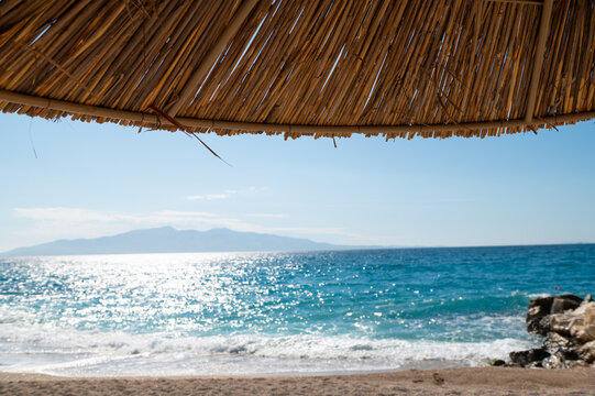 Sea view from beneath a thatched beach umbrella on a sunny daytime shore