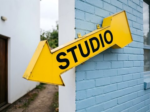 Yellow arrow sign pointing to a studio mounted on a blue brick wall