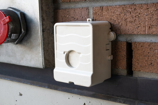 Wireless water meter module mounted on exterior brick wall. Remote endpoint device for monitoring and transmitting water usage data to utility provider. Selective focus.