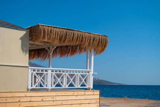 Thatched beach shelter with a white railing beside the sea in daylight