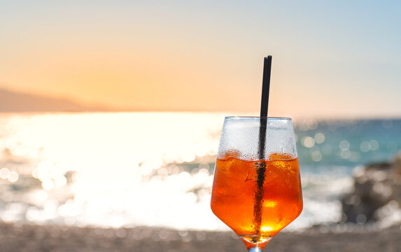 Orange cocktail with a straw on a seaside shore at sunset