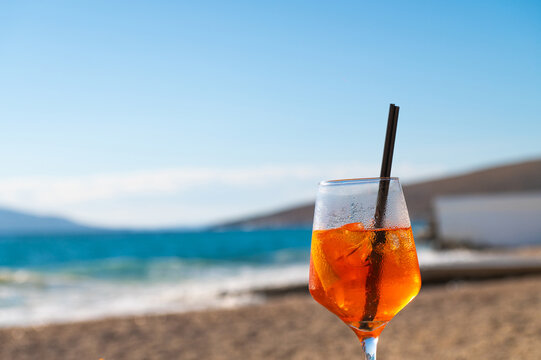 Orange aperitif with a straw on a beach overlooking the sea during the day