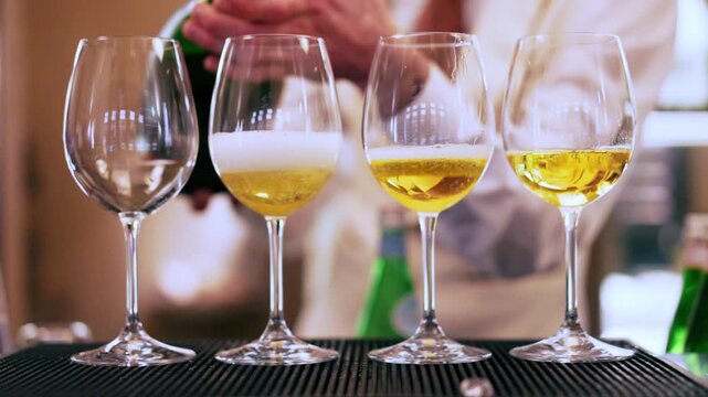 Bartender pouring fizzing champagne into the glasses standing in line on bar counter, professional barkeeper preparing refreshing drinks for aperitif party
