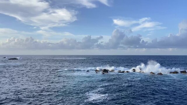 Ocean waves break over dark rocks beside a distant rocky island Roque de Garachico against blue cloudy sky in Tenerife, Canary Islands, Spain,4K.