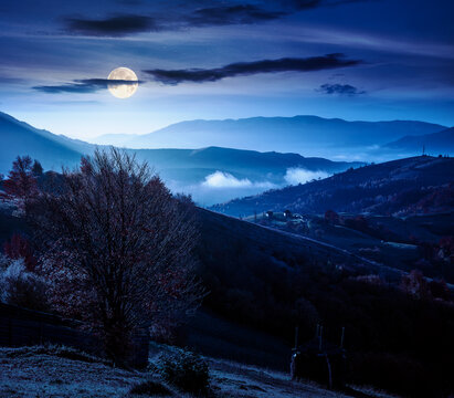 mountainous countryside landscape at night. full moon over dramatic sky above the distant valley. colorful fields and trees on the hill. mysterious nature landscape of Carpathians