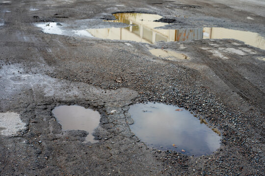 Potholes filled with rainwater on a damaged asphalt road. Cracked and deteriorating road surface in need of maintenance.