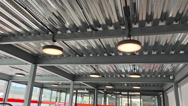 Modern industrial interior with galvanized steel beam ceiling, contemporary lighting and escalators leading into a spacious, empty transit hall or airport concourse