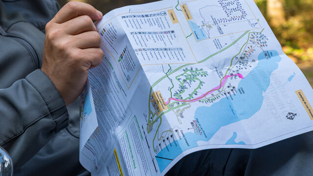 Hiker holding a folded illustrated map with colored routes and geographic details outdoors during a camping trip, close up