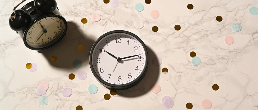 Two clocks on a beige marble surface with scattered confetti dots and copy space