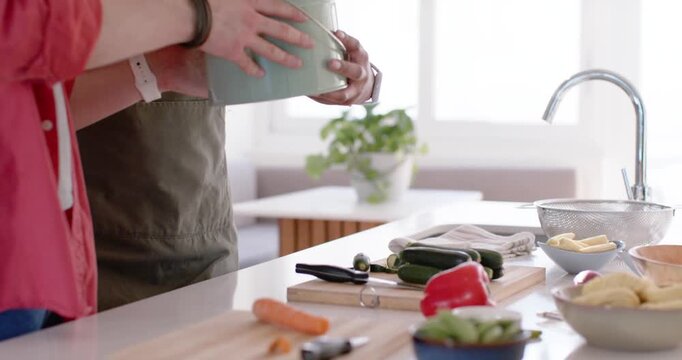 One is handing compost pail, partner is placing tin by sink for scraps while peeling carrots
