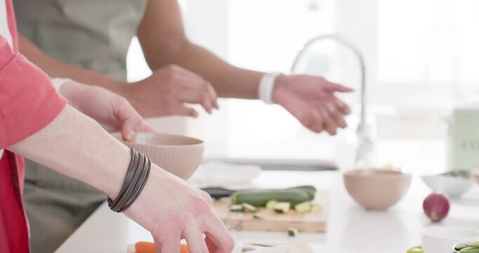At start, two people are scooping carrot slices into beige bowl and slicing zucchini