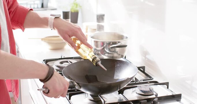 female cook steadying wok and pouring oil over low burner while pot steaming, preparing food