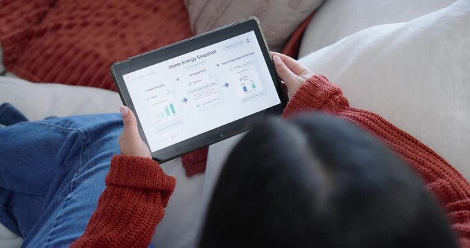 Person shifting grip and tapping tablet to check energy dashboard on couch, red throw nearby
