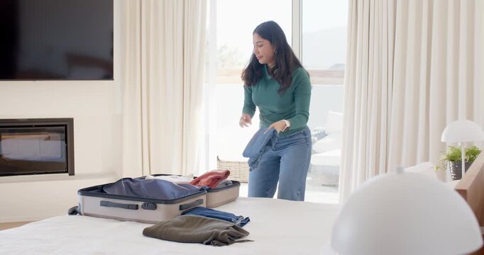 Woman entering bedroom, picking folded clothes from bed, inspecting and packing suitcase for trip