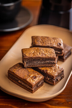 Stacked Homemade Chocolate Brownies on a Plate with Coffee Cup Close-Up in Cozy Cafe Setting