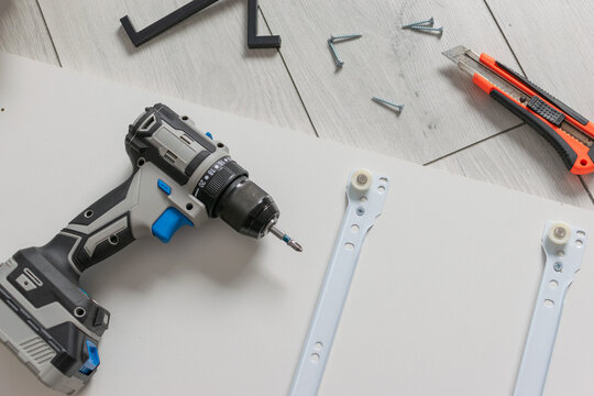 Assembling Furniture with Electric Drill, Screws, and Utility Knife on White Wooden Floor