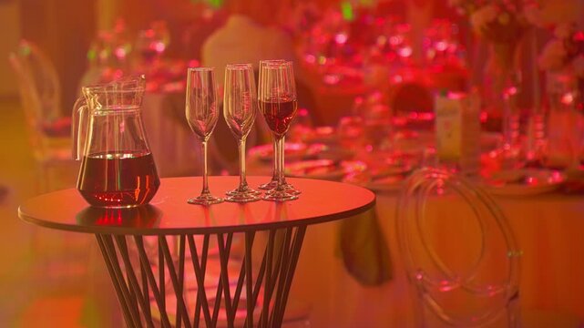 Champagne flutes and glass carafe on cocktail table. Green neon illumination at banquet party