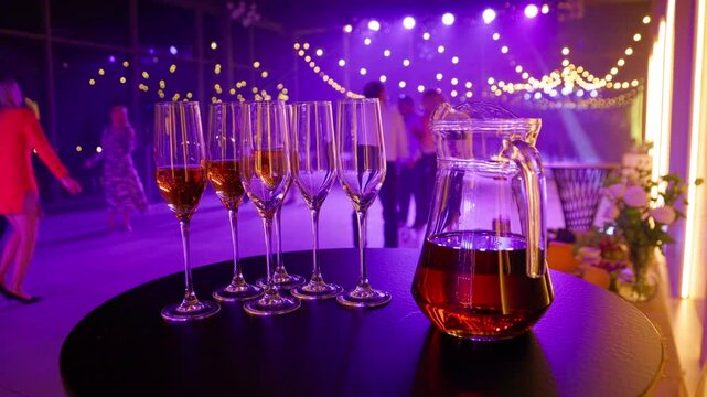 Welcome drinks in champagne flutes beside glass pitcher. People dancing under warm party lights