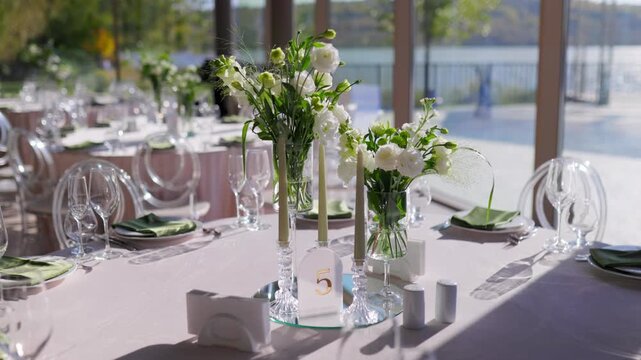 Wedding centerpiece of white flowers and tall candles on table. Lakeside restaurant venue view
