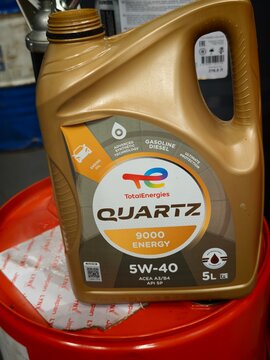 Russia, Sosnovy Bor, March 25, 2026 - TotalEnergies Quartz 9000 Energy 5W-40 motor oil in a 5L gold plastic canister. Synthetic engine oil, red bucket background, close-up.