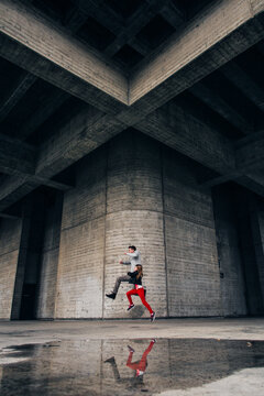 Father & Daughter jumping over a puddle surrounded by modern futuristic architecture building with stone and brick