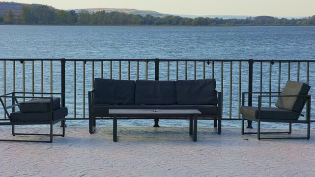 Lakeside terrace lounge with black sofa and armchairs. Outdoor restaurant patio overlooking water