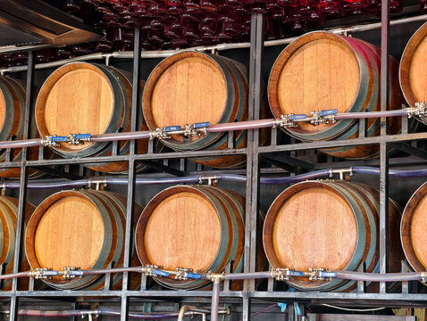 Wooden wine barrels with tubes and valves stand on a rack against a wall inside a wine drinking establishment, creating an authentic cellar atmosphere