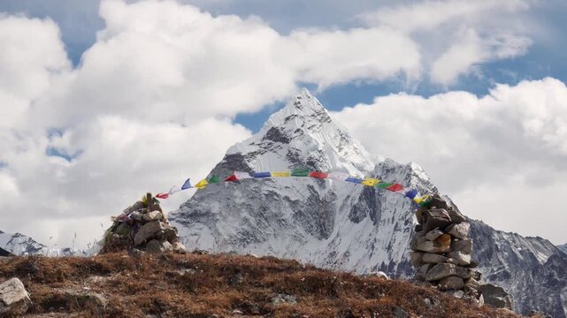 Majestic ama dablam mountain peak soaring into a cloudy blue sky in the himalayas, with traditional buddhist prayer flags on stone cairns fluttering in the wind in sagarmatha national park, nepal