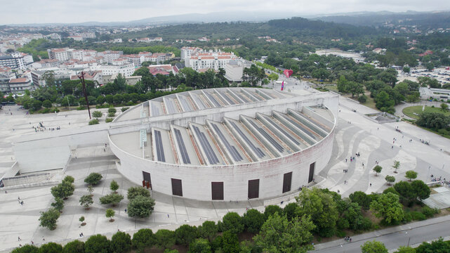 Aerial view of the Basilica of the Most Holy Trinity with circular architecture and tiered roof with solar panels, surrounded by paved sanctuary grounds in Fatima, Santarem District, Portugal.