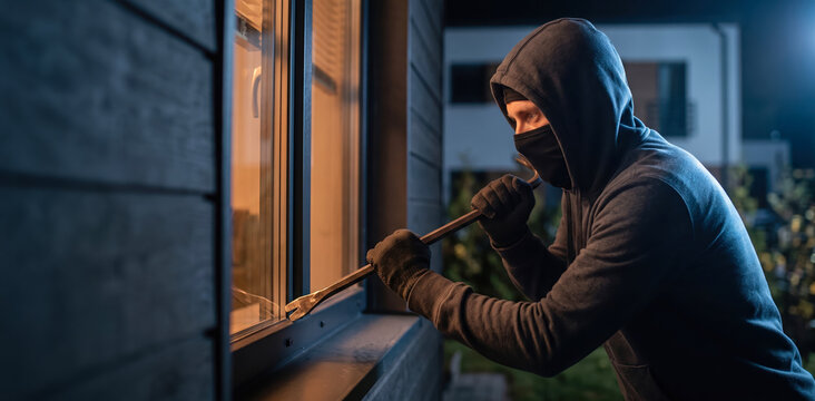 Burglar breaking into a residential house window at night using a crowbar