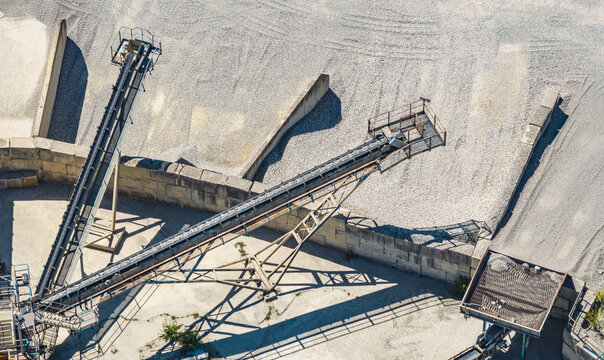 Aerial view of industrial conveyor belts above sorted gravel stockpiles separated by concrete retaining walls at an aggregate processing plant in Valence, Auvergne-Rhone-Alpes, France.