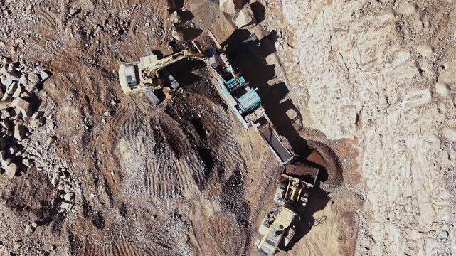 An excavator loads rock into haul trucks on the quarry floor, with tire tracks crossing the ground beside a high cut face.